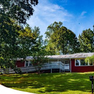 A charming red ranch-style house surrounded by lush green trees and a well-maintained lawn under a clear blue sky.