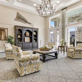 A spacious and elegantly decorated living room with armchairs, a chandelier, and large windows.