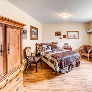 A cozy bedroom featuring a wooden armoire, bed, and chairs, with warm decor and wood flooring.