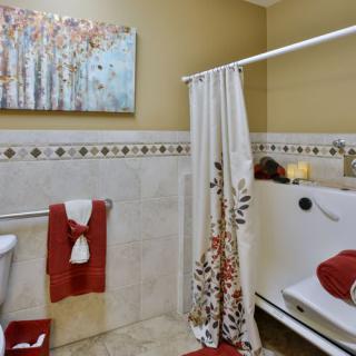 A well-decorated bathroom featuring a walk-in bathtub, decorative shower curtain, and neatly arranged towels with wall art.