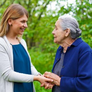 A younger woman and an elderly woman smiling and holding hands in a park.