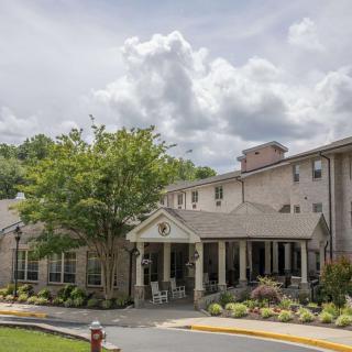 A residential building with a landscaped entrance, surrounded by trees under a cloudy sky.