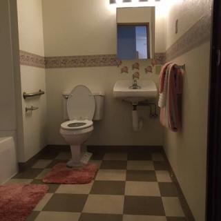 A bathroom with tiled flooring, featuring a toilet, sink, and mirror.
