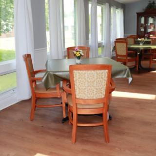 A cozy dining room with wooden chairs and tables set near large windows with flowing curtains.