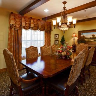 A traditional dining room with a wooden table and upholstered chairs, illuminated by a chandelier.