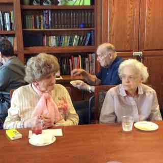 Elderly individuals are engaged in conversation at a social gathering in a library setting.