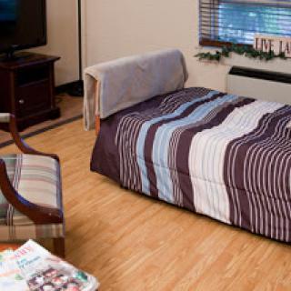A cozy room featuring a neatly made bed with a striped blanket, a comfortable chair, and a television.