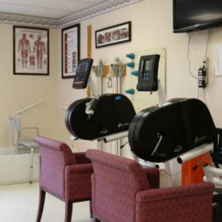 A fitness room featuring exercise machines and chairs, with anatomy posters on the walls.