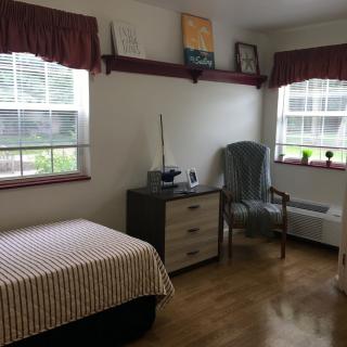 A cozy bedroom with a single bed, a chair, and two windows allowing natural light.
