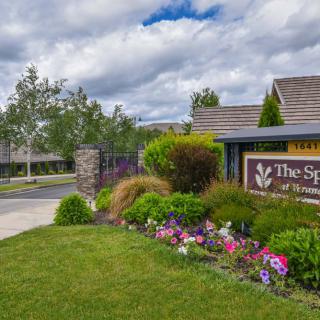 A landscaped entrance to 'The Springs' featuring a garden and sign under a cloudy sky.