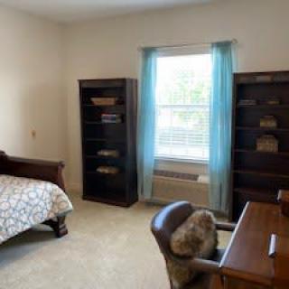 A cozy bedroom with a bed, two bookshelves, and a desk by the window.