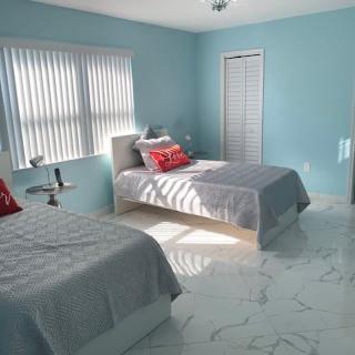 A bright bedroom with twin beds and minimalist decor, featuring blue walls and a marble floor.