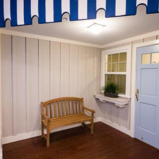 A cozy porch featuring a wooden bench and a blue door, with a striped awning overhead.