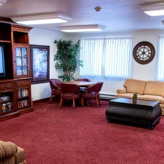 A cozy living room with a television, sofa, and a table surrounded by chairs on a red carpet.