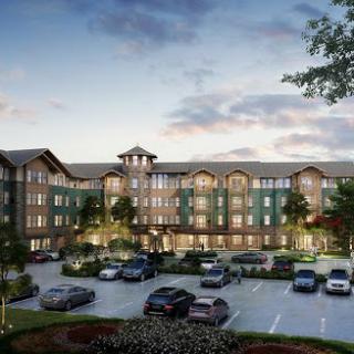 A modern residential apartment building at dusk, featuring ample parking and landscaped surroundings.