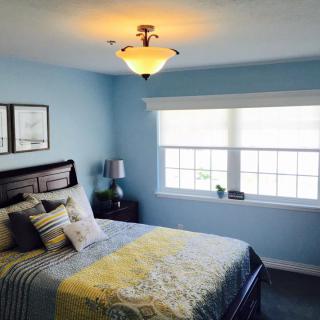 A cozy bedroom with blue walls, featuring a bed, nightstand, and large window.