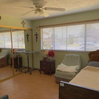 A cozy bedroom with a bed, mirror closet, and large windows with blinds.