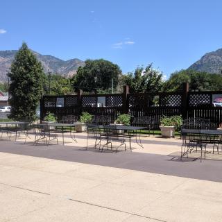 Outdoor seating area with tables and chairs, set against a backdrop of mountains under a clear blue sky.