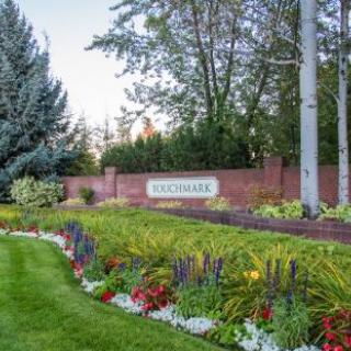 A beautifully landscaped garden with colorful flowers and lush greenery, framed by a brick wall and trees.