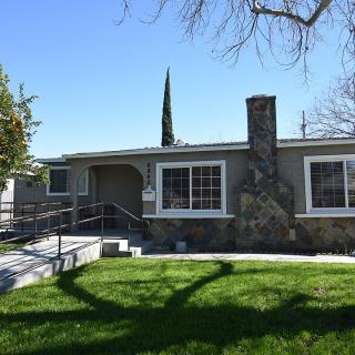 A single-story house with a stone chimney and well-maintained lawn under a clear blue sky.