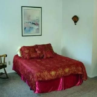 A cozy bedroom featuring a bed with red bedding, a wooden chair, and artwork on the wall.