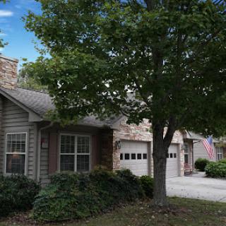 A charming residential home with a garage and lush greenery in the front yard.