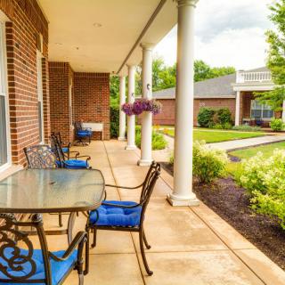 A cozy porch with a glass table and blue-cushioned chairs, overlooking a well-maintained garden.