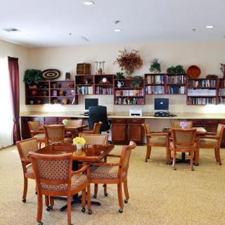 A cozy library room featuring bookshelves, computers, and tables with chairs.