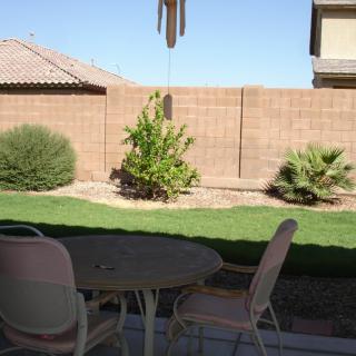A tranquil backyard patio with a table and chairs, surrounded by a well-maintained garden and grass.
