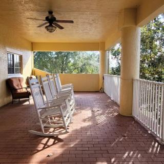 A spacious porch with rocking chairs and a ceiling fan, offering a relaxing view of the surrounding trees.