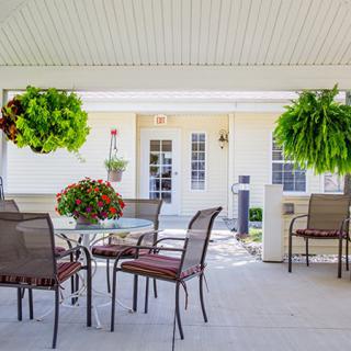 A cozy patio with outdoor seating arranged under a covered area, decorated with lush hanging plants.