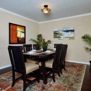 A stylish dining room featuring a large table with chairs, decorated with artwork and plants.