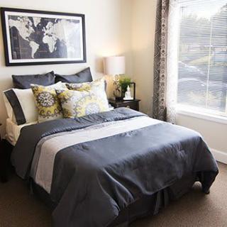 A cozy and stylishly decorated bedroom featuring a neatly made bed with patterned pillows, a bedside lamp, and a large window.