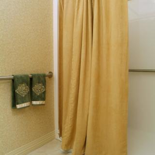A bathroom with a yellow shower curtain and green towels.