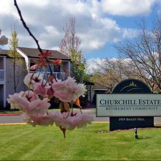 A scenic view of an apartment complex with spring blossoms in the foreground and a sign reading 'Churchill Estates'.