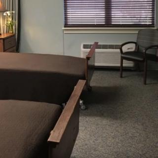 A hospital room with two beds and chairs near a window.