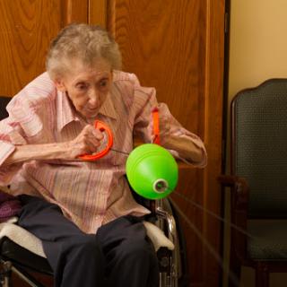 An elderly woman engaging in a rehabilitation exercise using a colorful toy while seated in her wheelchair.