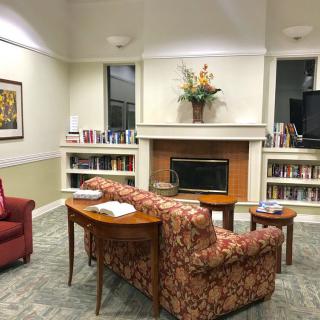 A cozy library reading room with a fireplace, bookshelves, and comfortable seating.