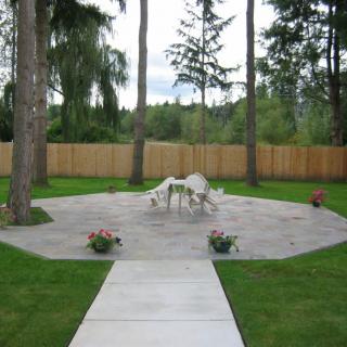 A serene backyard patio area with outdoor furniture surrounded by grass and trees.