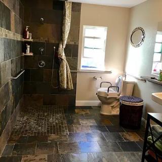 A spacious bathroom with tiled flooring, featuring a walk-in shower, toilet, sink, and mirror.
