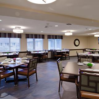 A neatly arranged dining area with tables and chairs, featuring modern lighting and large windows.