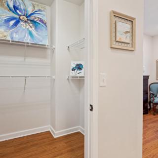 A small closet with wooden flooring, featuring artwork and shelves.