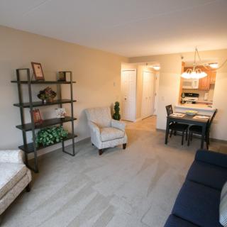A cozy living room with a dining area, featuring armchairs, a shelf, and warm lighting.