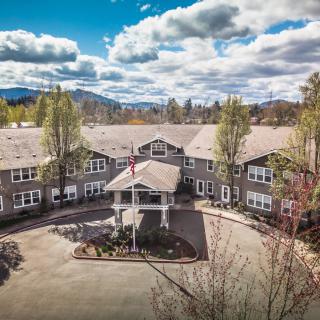 A large residential building surrounded by trees with a mountain backdrop under a partly cloudy sky.