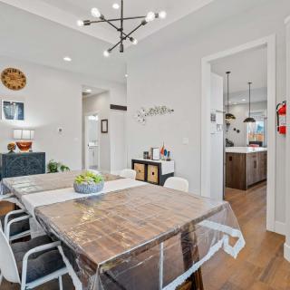 A modern dining room with a wooden table, contemporary lighting, and an open view into the kitchen.