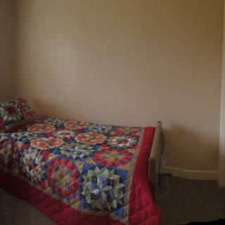 A simple bedroom with a single bed covered by a colorful quilt.
