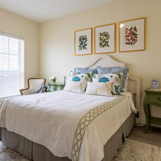 A cozy bedroom with elegant decor, featuring a neatly made bed, wall art, and natural light from a window.