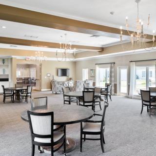 A spacious and elegantly designed dining area featuring round tables, chairs, and chandeliers.