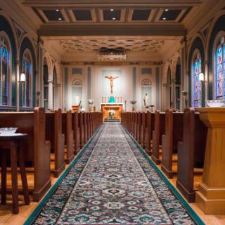 The interior of a beautifully designed church with a central aisle leading to the altar, flanked by rows of wooden pews.