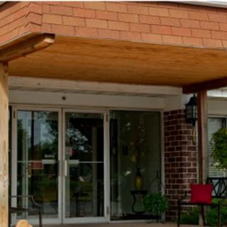 The image shows the entrance of a building with glass doors and a wooden canopy, complemented by brick walls and outdoor seating.